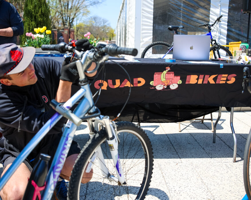 A member of the Quad Bikes student grant project helps fix a student's bike during an Earth Day celebration.