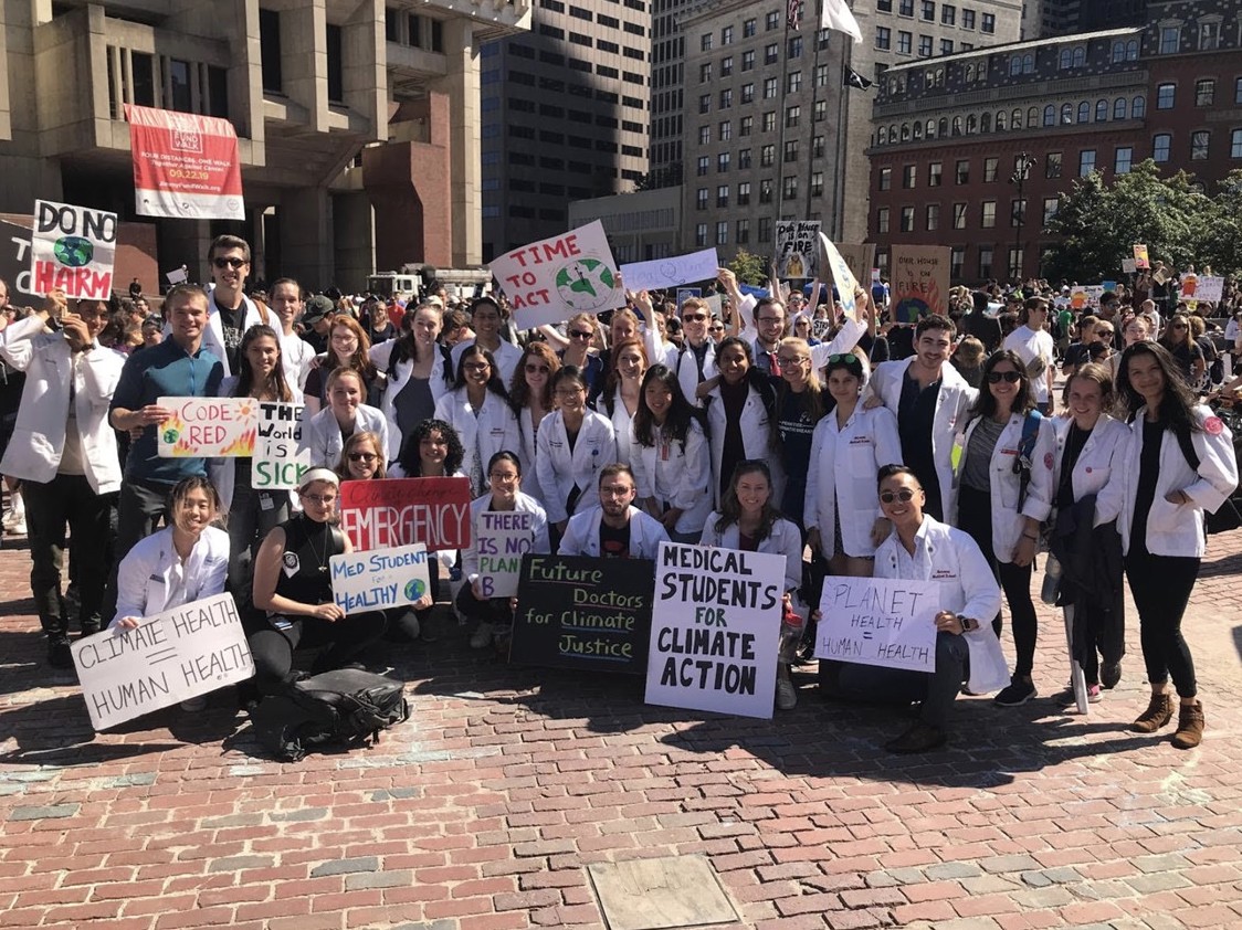Dozens of Harvard students pose for a photo at a protest with signs that advocate for human health as part of climate health.