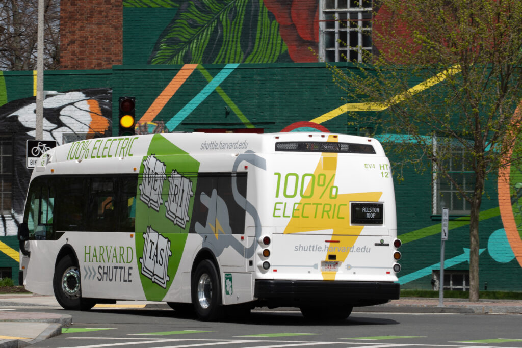 An electric shuttle bus from Harvard drives past a mural.