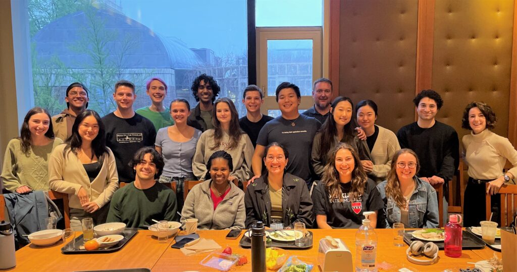 A group photo of REP student members posing at a long wooden table. 