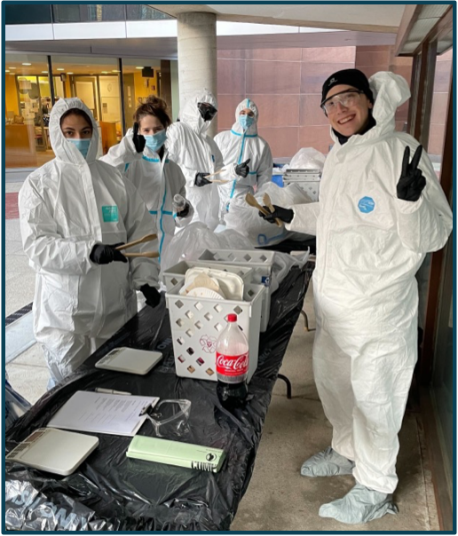 REP student group members wear hazmat suits while conducting a waste audit. They smile and pose for a photo.