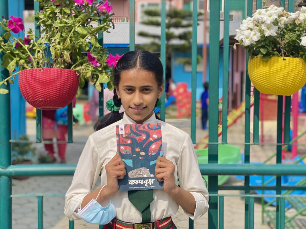A young student in front of a playground smiles and holds the Climate Change Workbook.